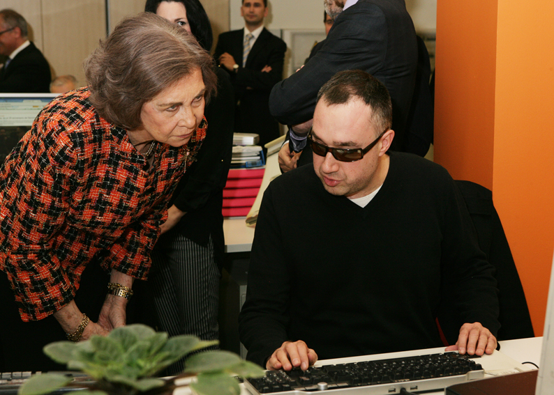 Doña Sofía atiende las explicaciones de un redactor afiliado a la ONCE