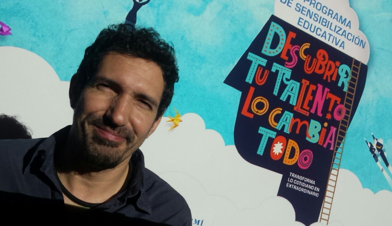 El docente César Bona posa ante el cartel promocional del 32 Concurso Escolar de la ONCE y su Fundación