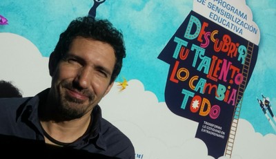 El docente César Bona posa ante el cartel promocional del 32 Concurso Escolar de la ONCE y su Fundación