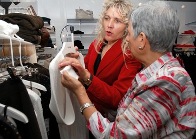 Una voluntaria ayuda a escoger un vestido a un afiliada en una tienda de confección