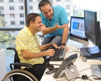Un trabajador con discapacidad física frente a su ordenador y junto a un compañero