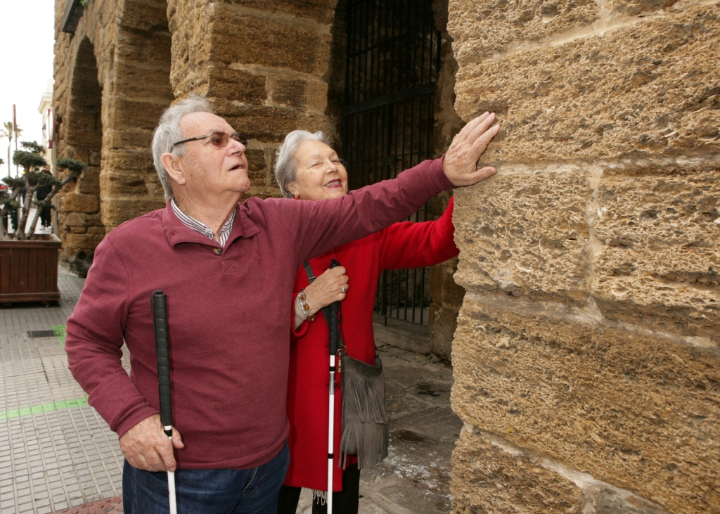 Una pareja de afiliados reconoce al tacto los muros de un edificio histórico en Cádiz