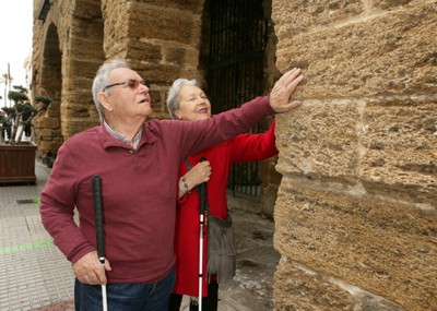 Una pareja de afiliados reconoce al tacto los muros de un edificio histórico en Cádiz