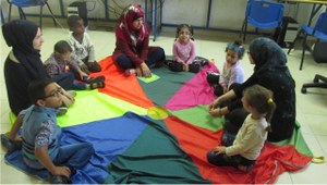 Un grupo de seis niños ciegos y tres profesoras en una actividad lúdica de reconocimiento de colores, sentados en el suelo del aula