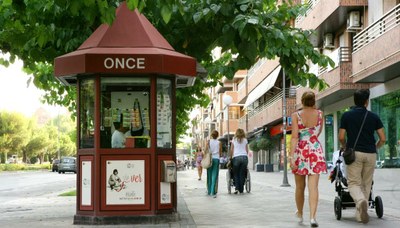 Imagen urbana de un grupo de ciudadanos paseando por delante de un kiosco de la ONCE