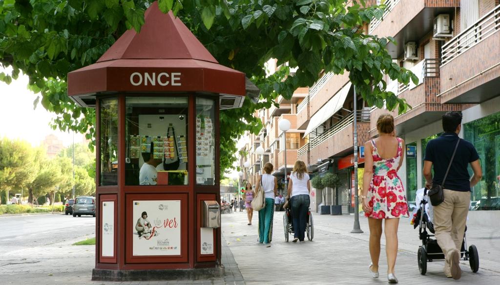 Imagen urbana de un grupo de ciudadanos paseando por delante de un kiosco de la ONCE