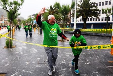 Una persona mayor cruza la meta bajo la lluvia junto a su acompañante, un niño provisto de antifaz que le impedía la visión