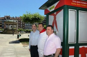 El delegado territorial, Jesús Buitrago (a la izquierda), y el presidente del Consejo navarro, Valentín Fortún, flanquean a uno de los vendedores del cupón junto a su kiosco decorado al efecto, y él también con el traje tradicional sanferminero
