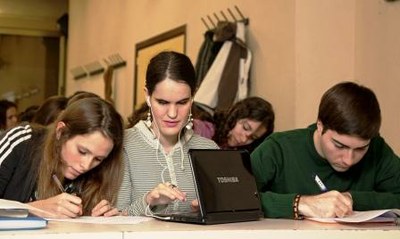 Una joven ciega universitaria toma apuntes en su ordenador adaptado, flanqueada en clase por dos compañeros 