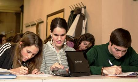 Una joven ciega universitaria toma apuntes en su ordenador adaptado, flanqueada en clase por dos compañeros 