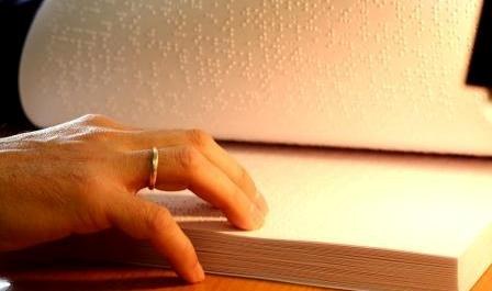Una persona posa sus dedos sobre el  texto en braille de un libro