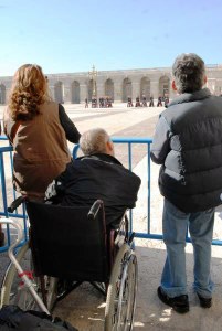 Una persona en silla de ruedas observa, junto a dos acompañantes, una parada militar en el Palacio de Oriente de Madrid