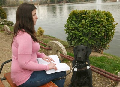 Mujer ciega leyendo braille en un parque público junto a su perro guía