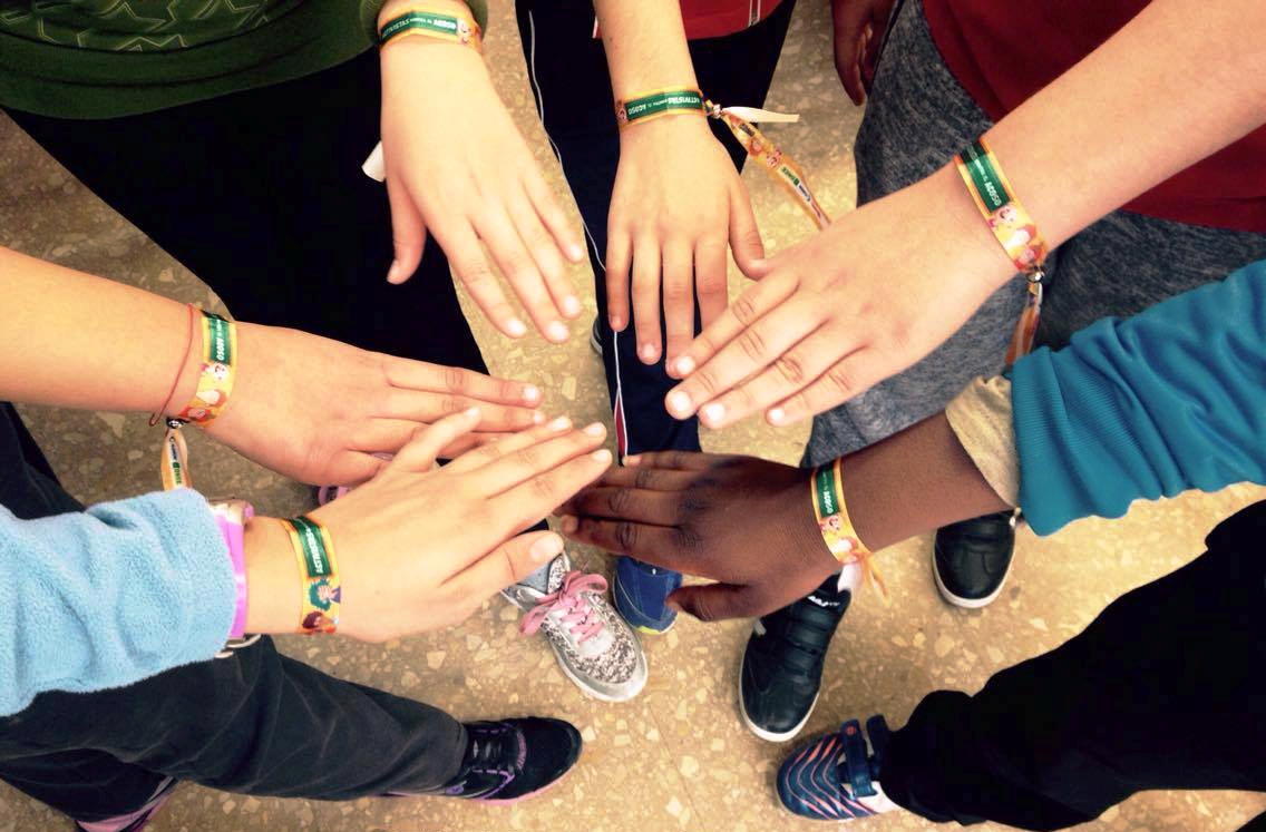 Un grupo de niños de diferentes razas unen sus brazos ataviados con las pulseras contra el acoso que distribuye el Concurso Escolar entre todos sus participantes