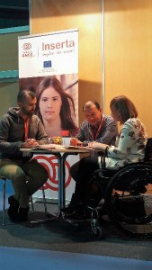 Una pareja de jóvenes (ella en silla de ruedas) conversa con un técnico de Inserta Empleo