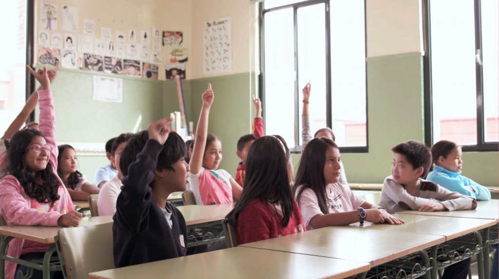 Una votación de niños, de procedencia diversa, vota a mano alzada una proposición en el aula