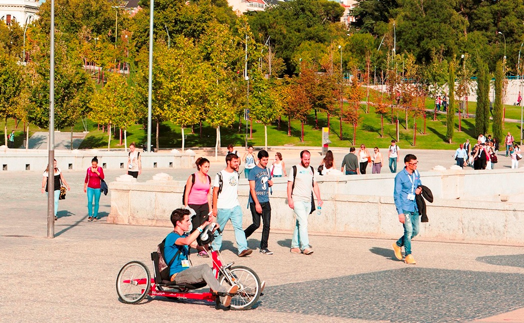 Un joven con discapacidad se mueve en su ciclo-silla sobre ruedas por un campus universitario