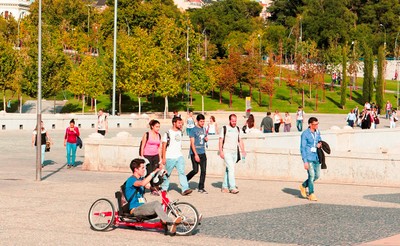 Un joven con discapacidad se mueve en su ciclo-silla sobre ruedas por un campus universitario