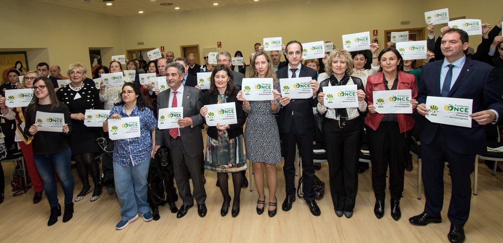 Todos los asistentes al acto muestran el cartel de la campaña