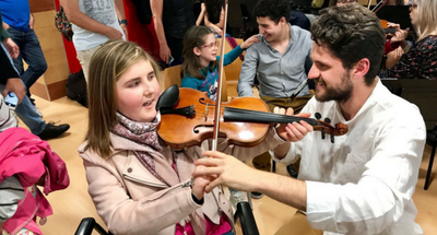 Uno de los profesores de la UAX muestra a una niña afiliada cómo situar el violín para tocarlo