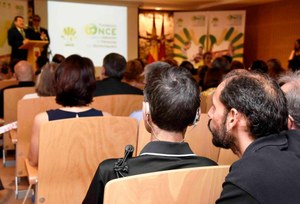 Un sordociego atiende entre el público al acto celebrado en Murcia, mientras -tras él- un mediador le ayuda a seguir la sesión