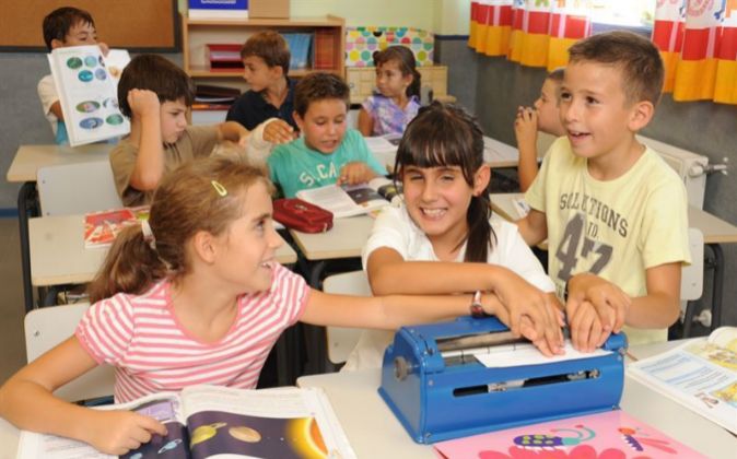 Una niña ciega muestra a dos compañeros de aula un texto en braille que ha escrito en su máquina Perkins