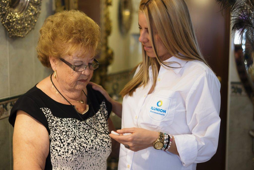 Una técnico de ILUNION Sociosanitario enseña a una señora mayor la utilización del dispositivo de teleasistencia