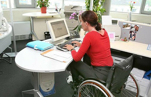 Una trabajadora con discapacidad, frente a su ordenador, sentada en su silla de ruedas