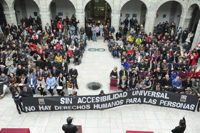 Miembros de los colectivos de CERMI Cantabria, reunidos, con su pancarta reivindicativa, en el pario del Parlamento autonómico