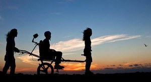 Dos personas ayudan a trasladarse en un entorno rural a una tercera en silla de ruedas