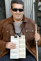 Imagen de un vendedor de la ONCE, con sus cupones y el bastón blanco