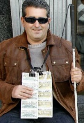 Imagen de un vendedor de la ONCE, con sus cupones y el bastón blanco