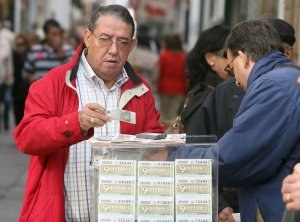 Un cliente adquiere un cupón a un vendedor de la ONCE en una concurrida escena urbana
