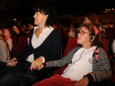 Una niña con discapacidad visual escucha, mediante sus cascos, la audiodescripción de un espectáculo en una sala de teatro