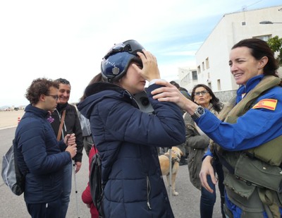 Rosa Mª García, la primera mujer piloto española de cazas, ayuda a probarse el casco a una joven ciega
