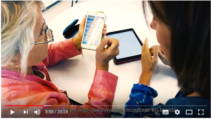 Una instructora explica a una afiliada mayor el funcionamiento de una aplicación de su smartphone en una imagen capturada del vídeo