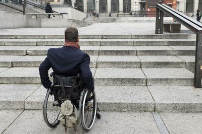 Persona en silla de ruedas ante una escalinata en la vía pública