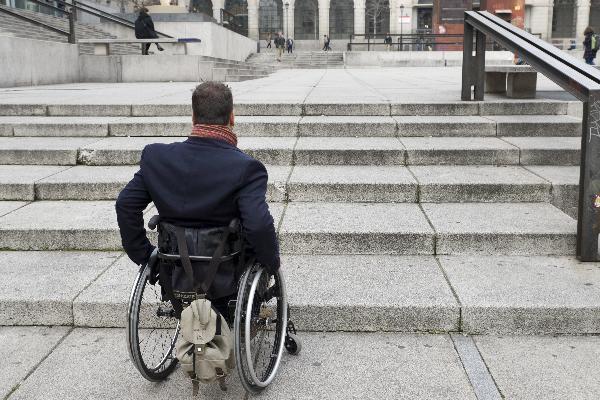 Persona en silla de ruedas ante una escalinata en la vía pública