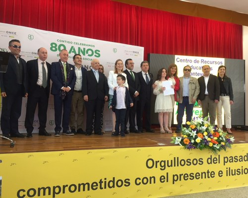 Foto de familia, sobre el escenario, de autoridades y participantes en el acto institucional de la jornada festiva 
