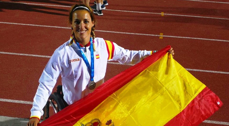Eva Moral pasea sobre su silla por la pista de atletismo portando la bandera española