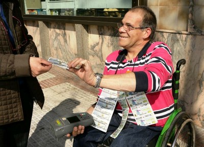 Un vendedor de la ONCE, provisto de su TPV, entrega a una cliente un producto de juego