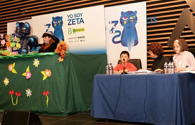 Los dos pequeños afiliados (a la derecha) dan lectura al cuento, mientras junto a ellas se representa la historia con marionetas