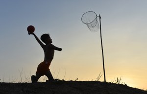 Tercer premio, un niño con amputación en ambas piernas y en un brazo jugando al baloncesto con una improvisada canasta en el campo