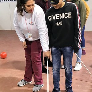 Una monitora muestra a un joven con los ojos tapados con un antifaz como intentar moverse valiéndose de la ayuda de un bastón blanco