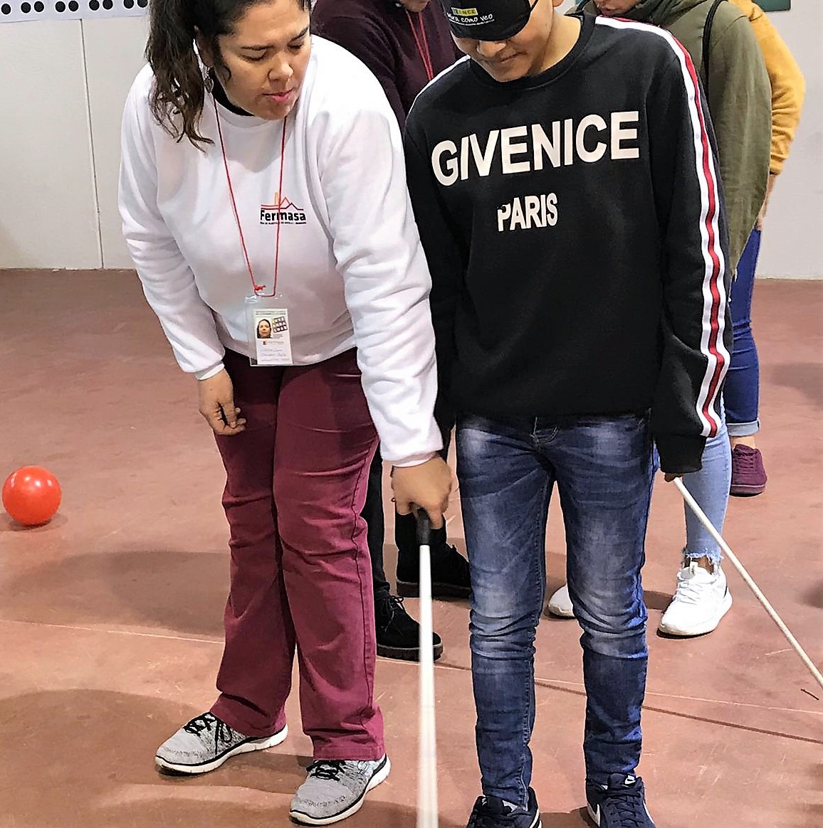Una monitora muestra a un joven con los ojos tapados con un antifaz como intentar moverse valiéndose de la ayuda de un bastón blanco