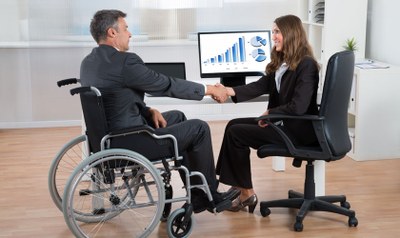 Persona en silla de ruedas saludando a una compañera en su empresa de trabajo