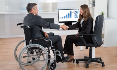 Persona en silla de ruedas saludando a una compañera en su empresa de trabajo