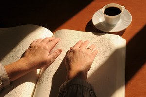 Una mujer lee un libro braille junto a una taza de café