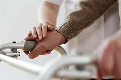 La mano de una cuidadora fija la de una persona mayor en el andador que le sirve para desplazarse