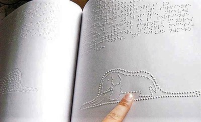 Unas manos recorriendo las páginas de un libro impreso en braille con ilustraciones en relieve producido por el SBO